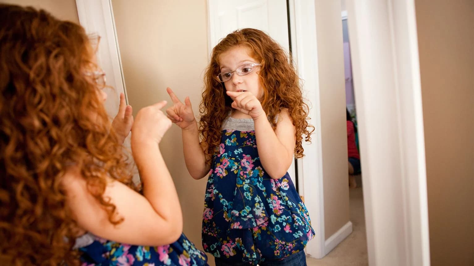 A little girl talking to herself in front of a mirror